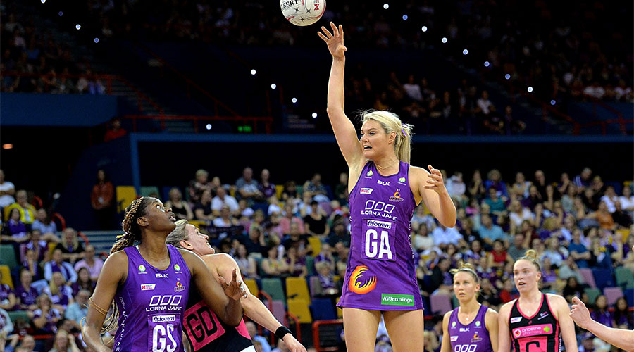 Gretel Tippett jumping in the air with the ball to pass to Romelda Aiken